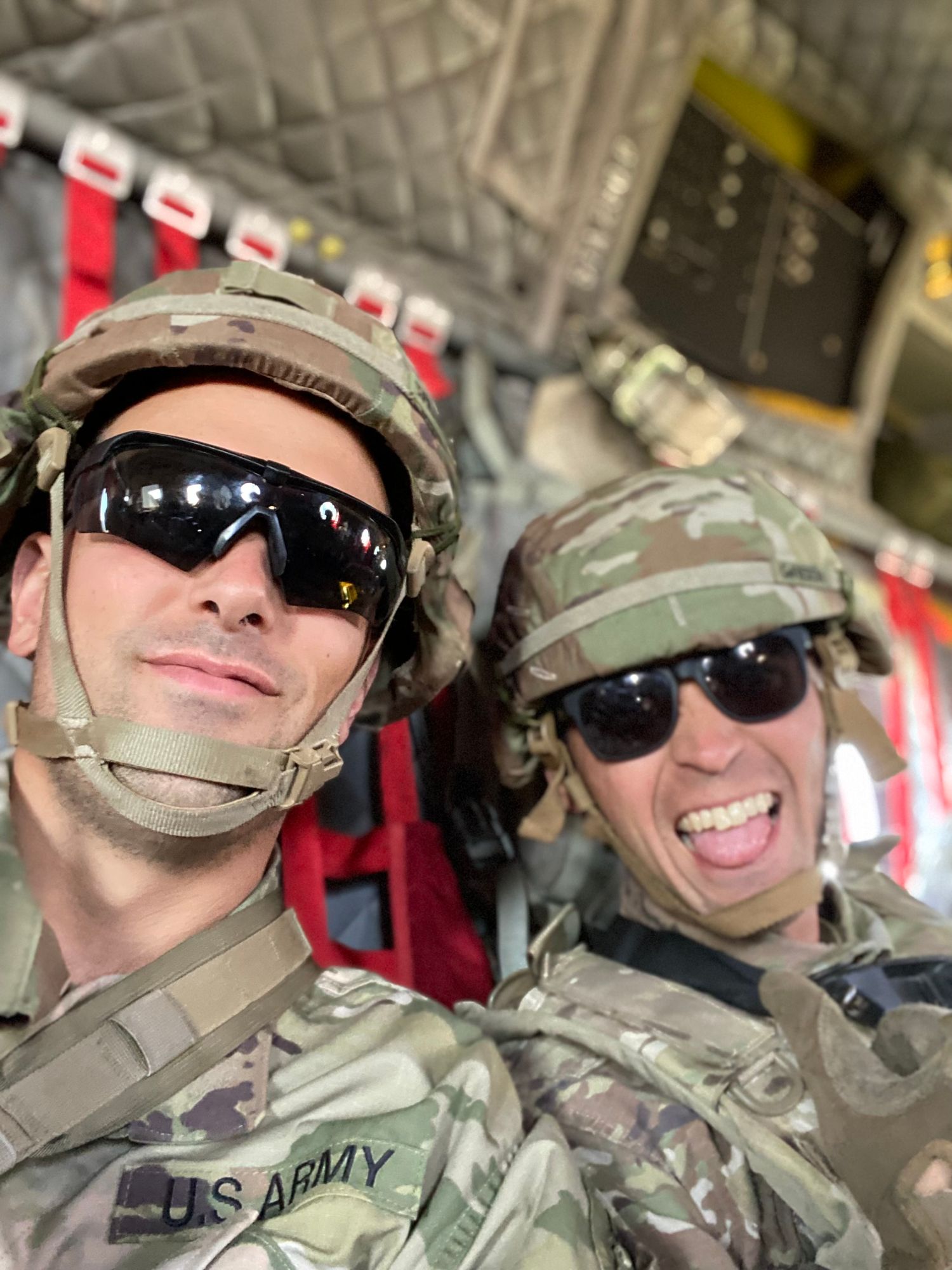 Two soldiers in camouflage uniforms and sunglasses pose together inside what appears to be a military aircraft.