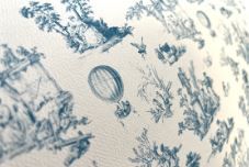 Closeup of blue and white toile fabric pattern with a hot air balloon design detail against a light background.