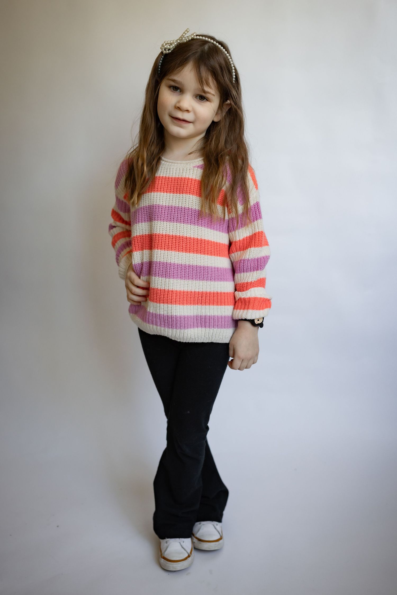 Young girl in a multicolor striped sweater and black flare pants wearing a decorative headband.