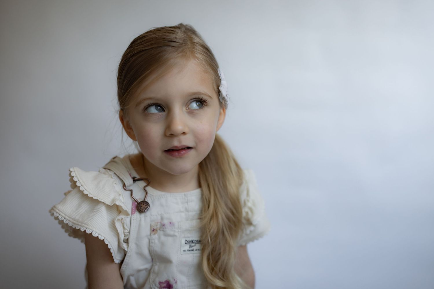 Blonde girl in ruffled floral top with side ponytail gazes upward thoughtfully.
