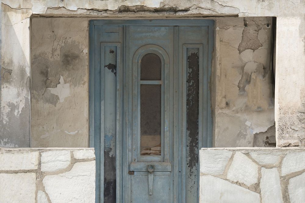 A weathered light blue wooden door with arched details set in a stone wall facade shows signs of aging and character.