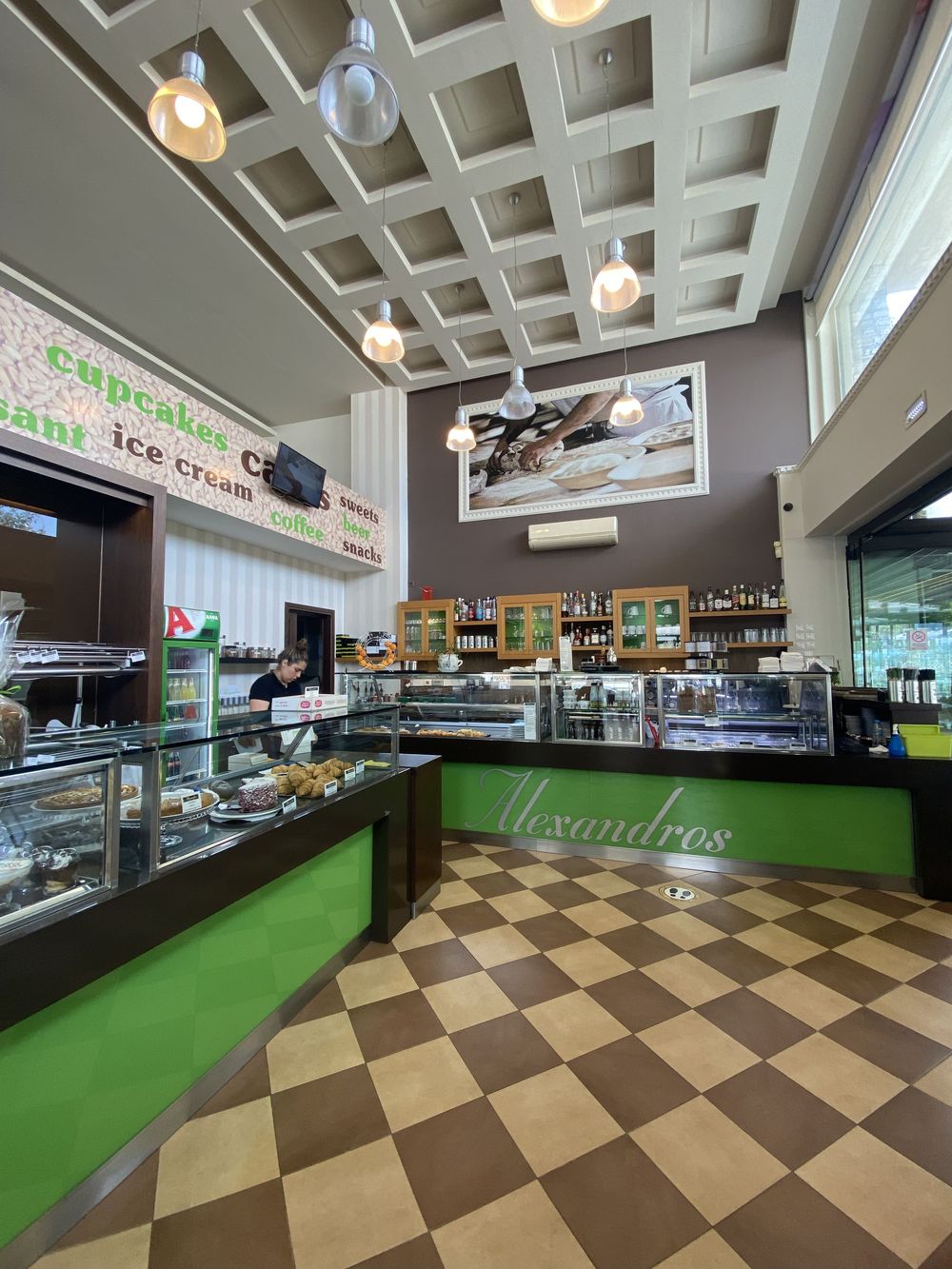 Interior view of a modern deli counter with green floors and checkered brown tiles showing multiple display cases.