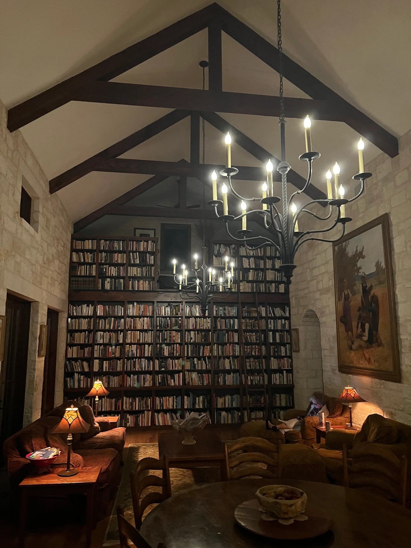 Cozy library room with dark bookshelves, exposed beams, and modern chandelier lighting creating a warm ambiance.