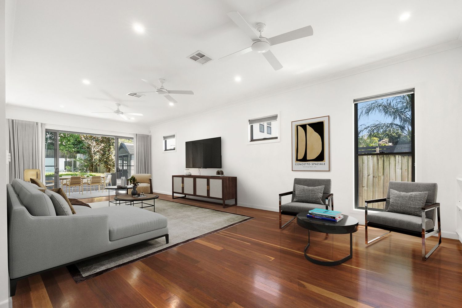 Spacious living room with polished hardwood floors, grey sofa, ceiling fans, and large windows.