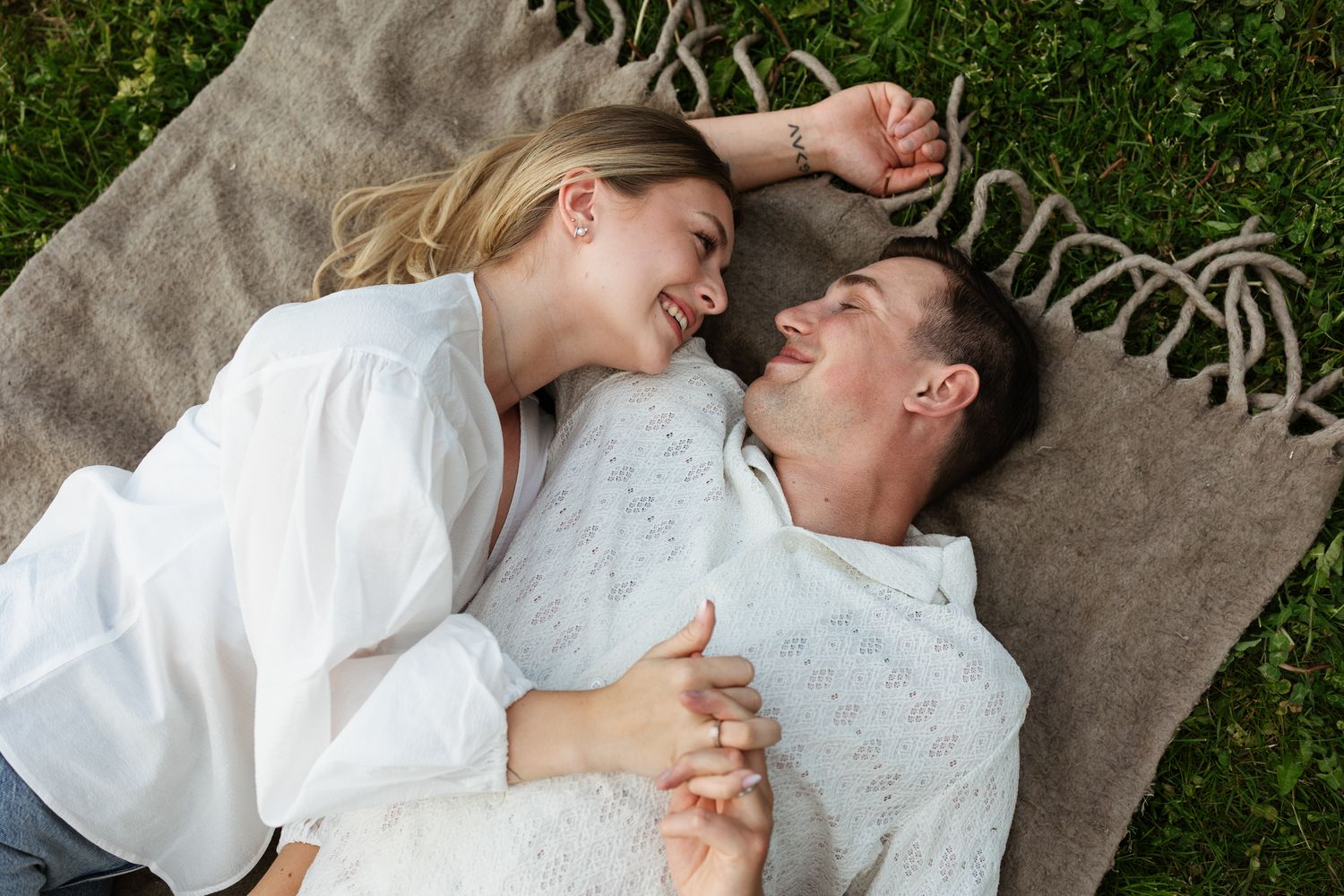 A couple in white clothing lies on a stone surface outdoors while sharing a romantic moment together.