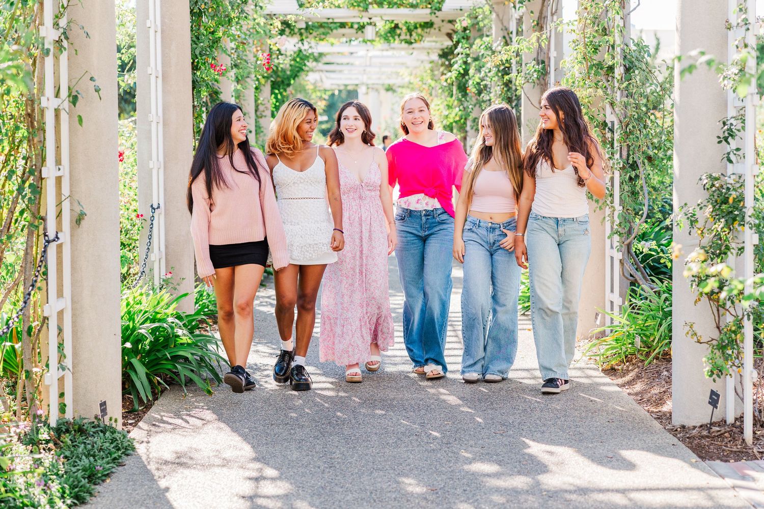 A group of friends in colorful dresses and casual attire pose together outdoors on a sunny day.