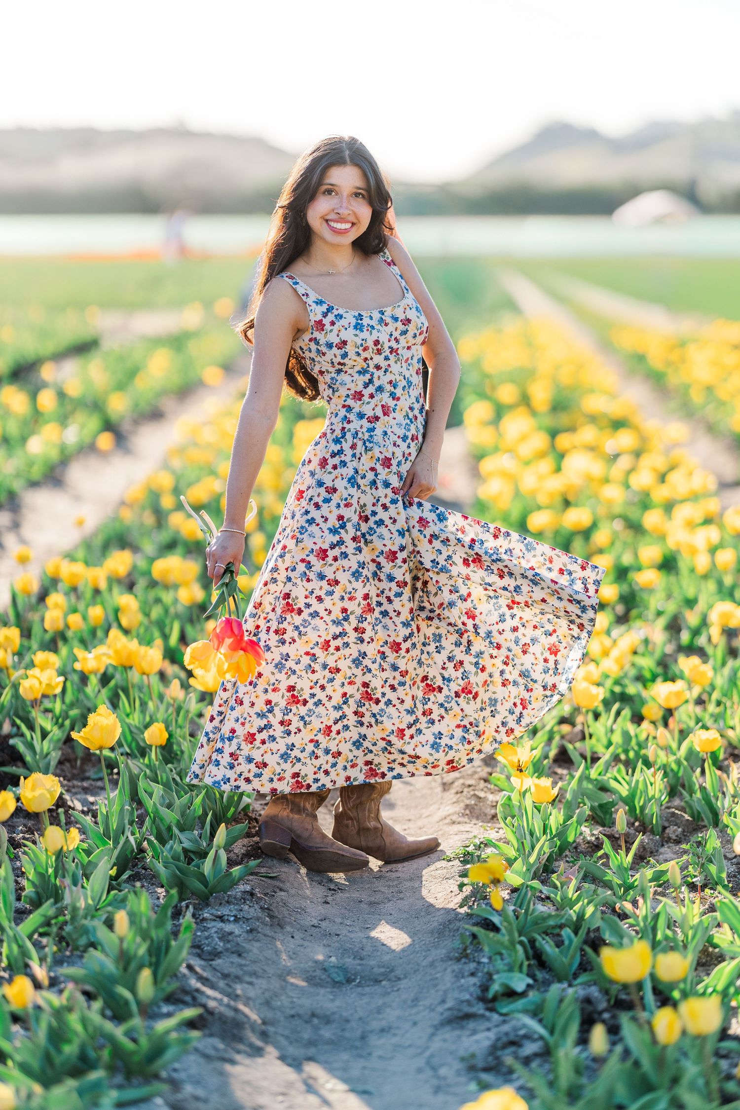 A person in a floral dress twirls among vibrant yellow tulip fields on a sunny spring day.