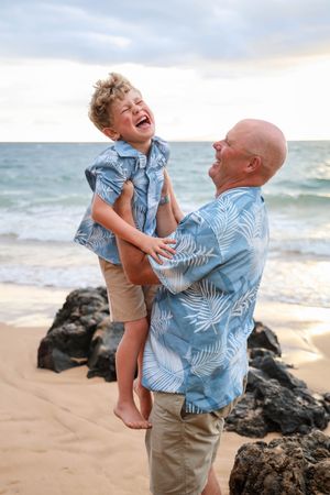 A playful moment between two people laughing and embracing on a rocky beach at sunset.