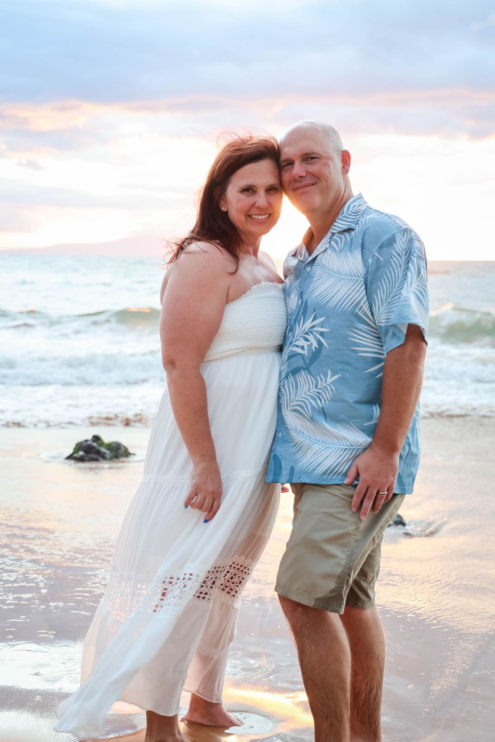 A couple in white and blue outfits share romantic moments on a beach at sunset, captured in multiple poses.