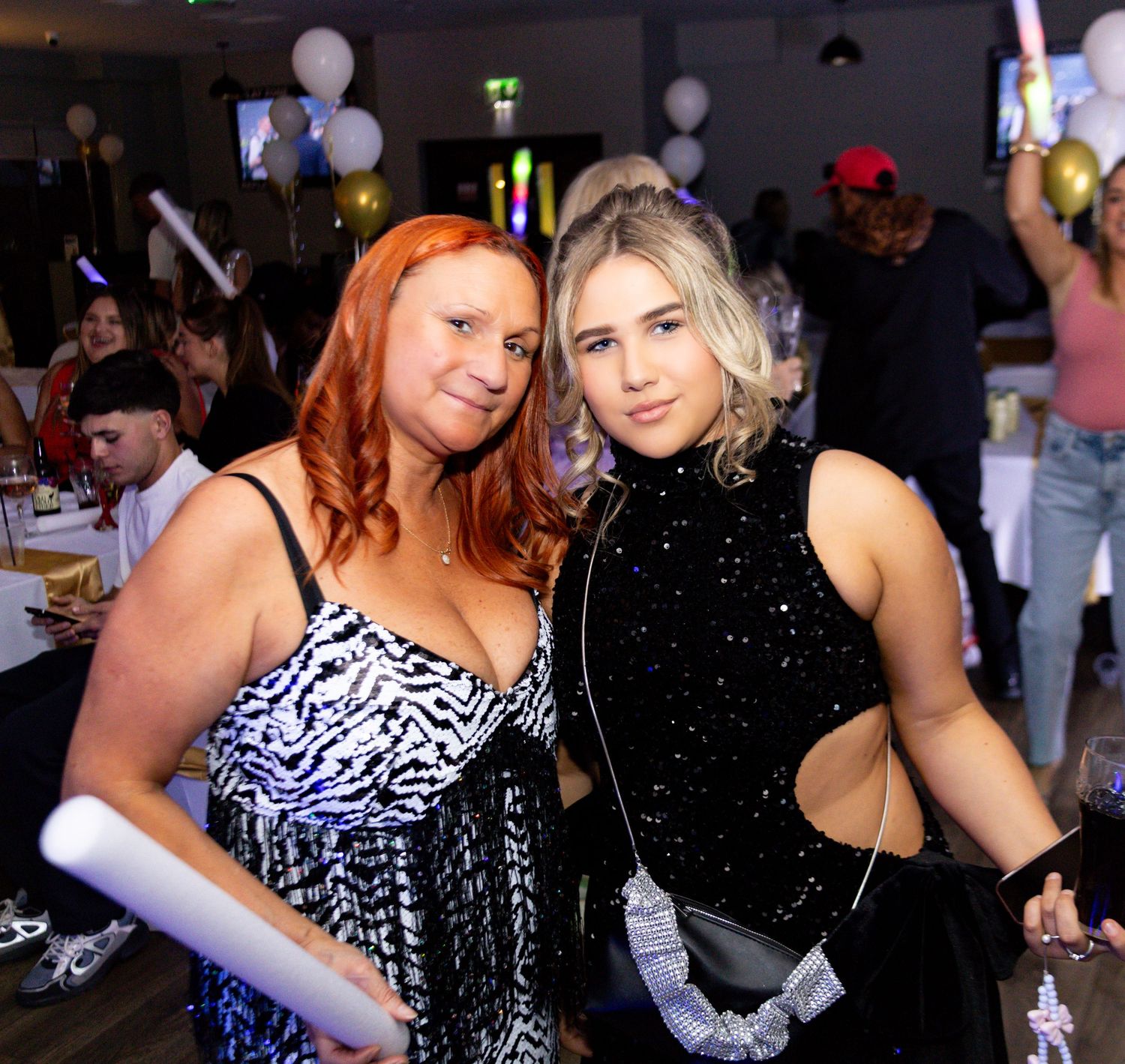 Two women pose together at a party, one wearing a zebra print dress and one in a black sparkly cutout dress.