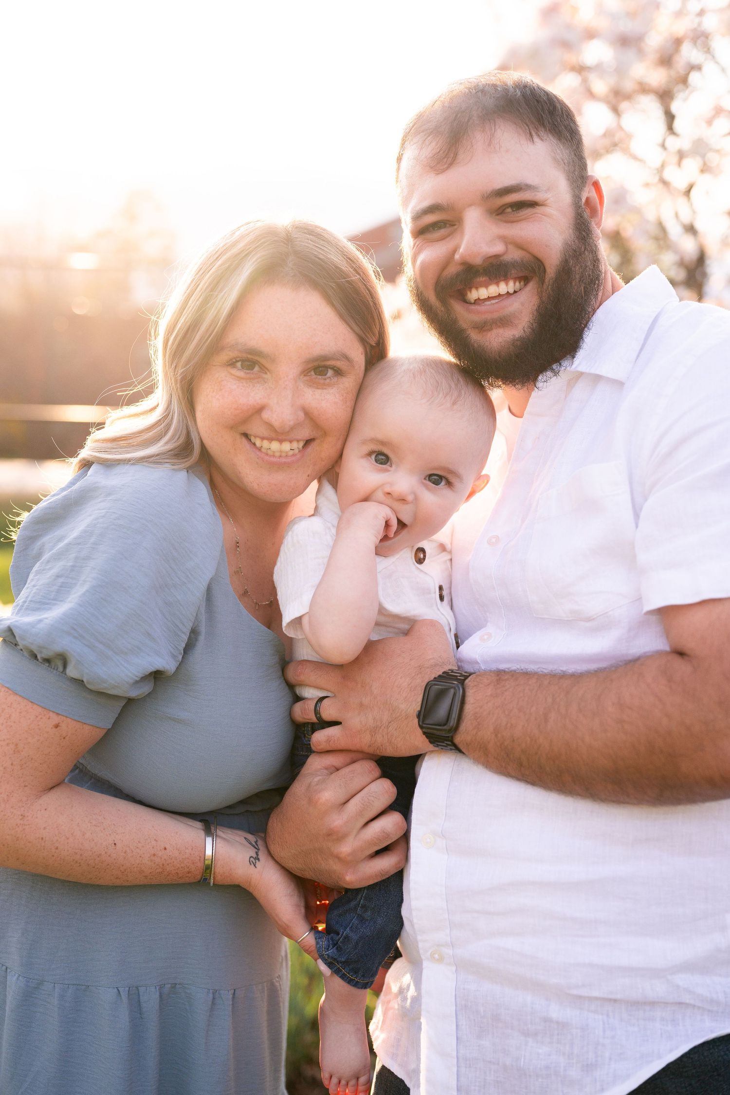 A family poses together outdoors during golden hour sunset with warm backlighting creating a glowing effect.