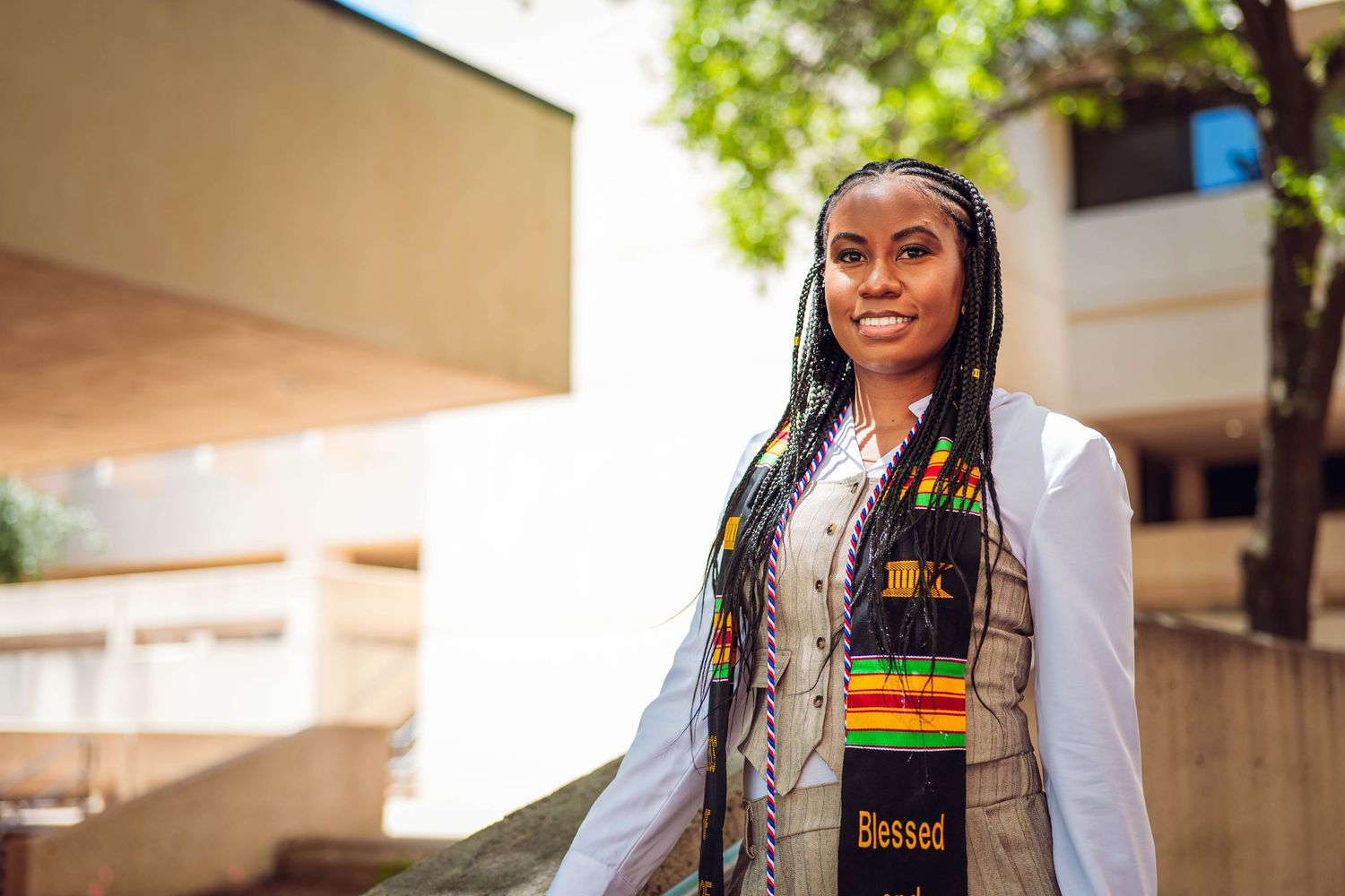 Student wearing graduation stole and accessories poses on campus. UTD Graduate Portraits by Eric Aaberg Photography in DFW.