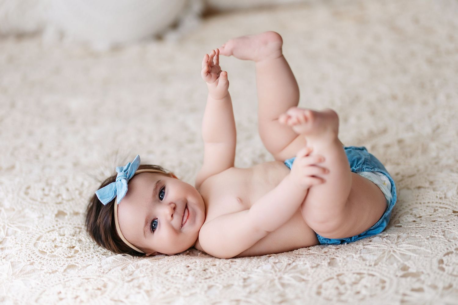 A baby in blue denim lies on a light carpet in a series of progressive developmental milestone poses.