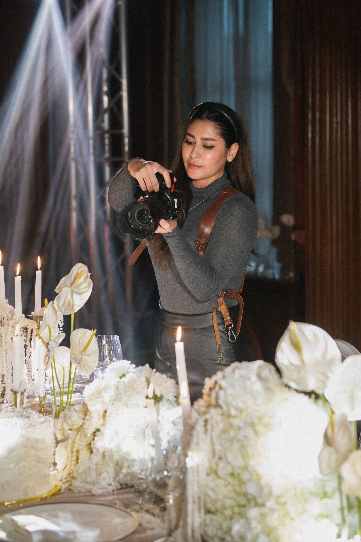 Female wedding photographer capturing white floral centerpiece details at elegant candlelit reception table setup.