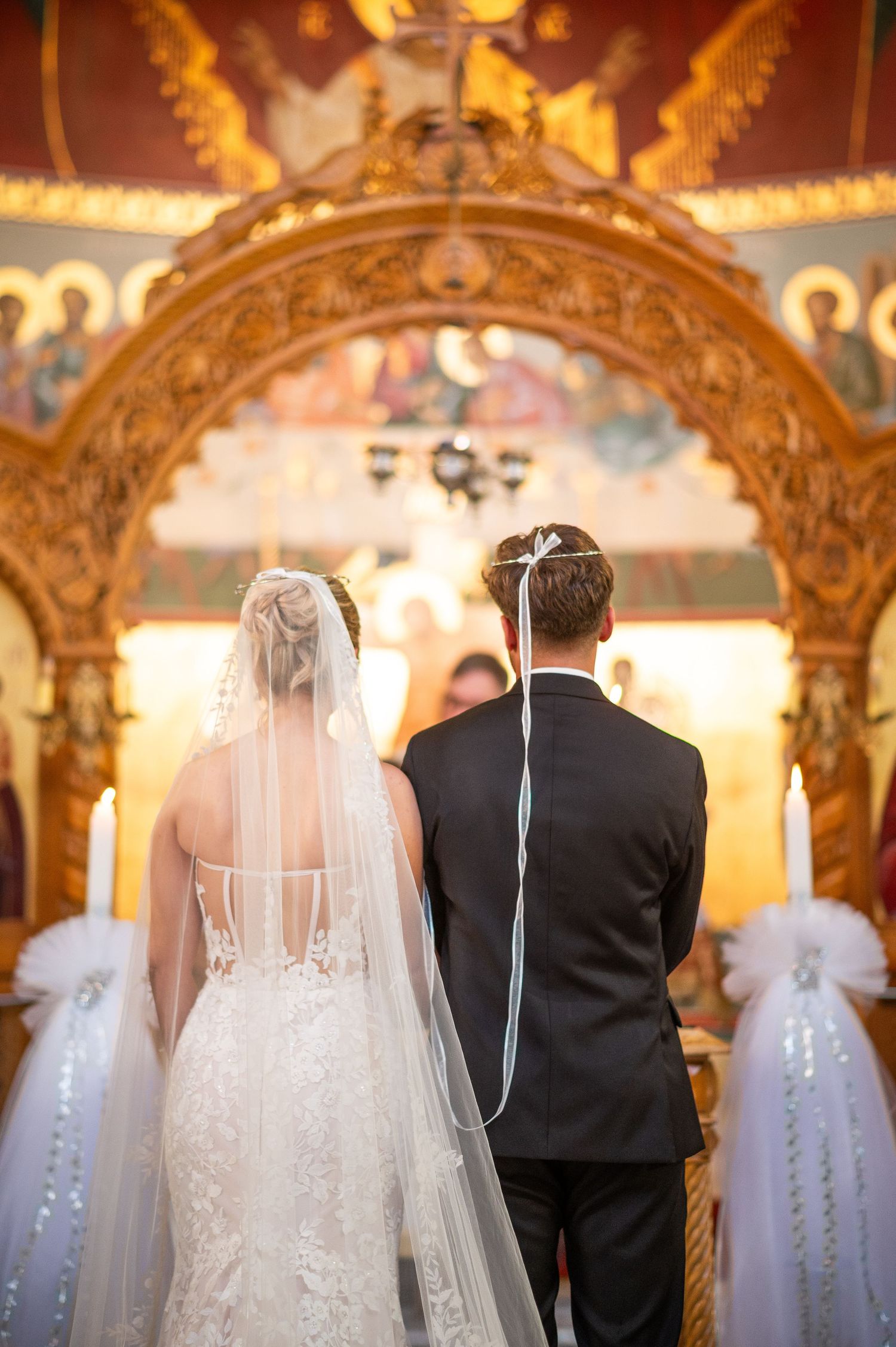 A bride and groom stand at the altar in an ornate church with golden arches and decorative details during their wedding ceremony.