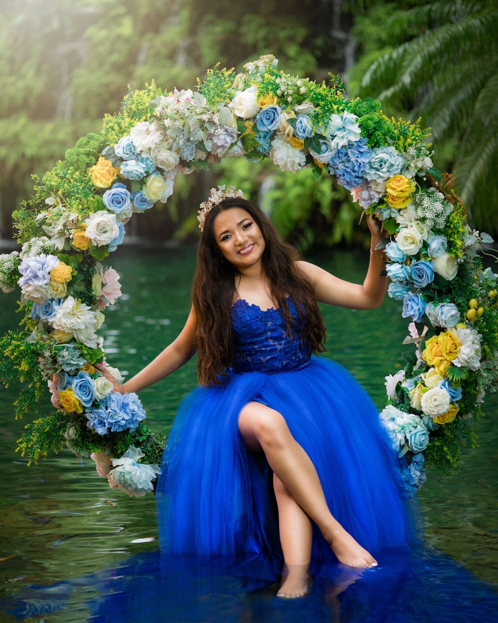 Quince Girl in royal blue ball gown sitting on a floral wreath swing over a tranquil lake.