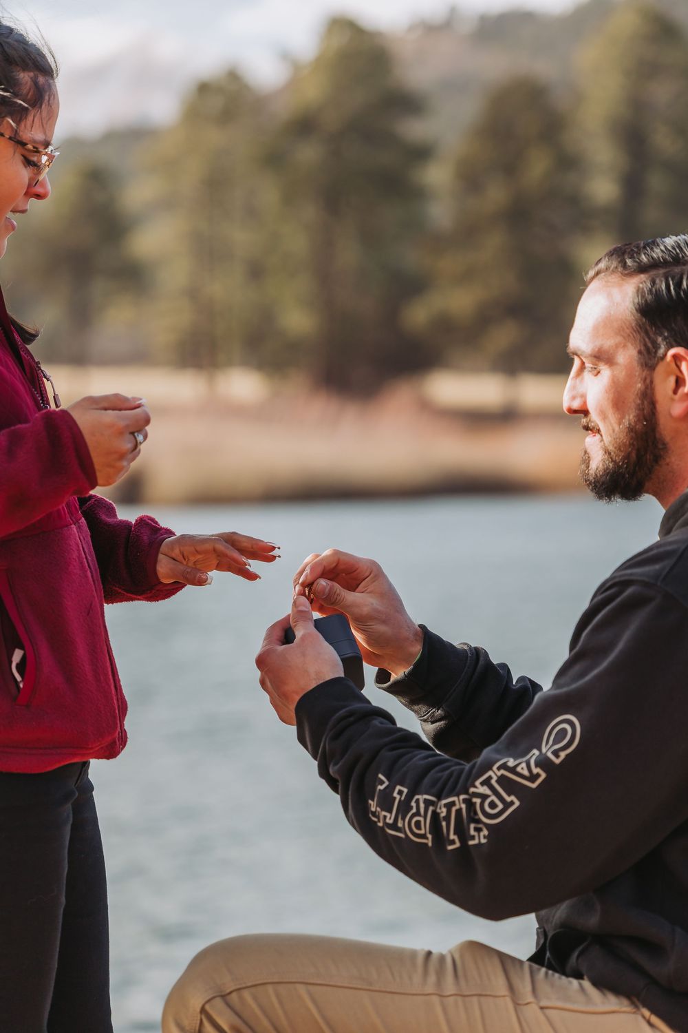 Two people share a romantic moment by a lake during a marriage proposal with a ring.