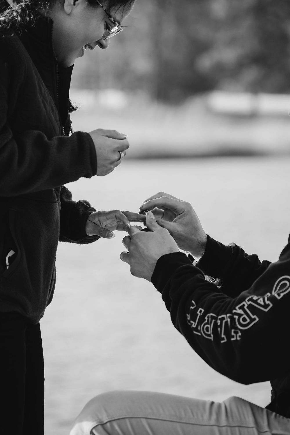 Black and white close-up image showing hands exchanging something in an outdoor setting.