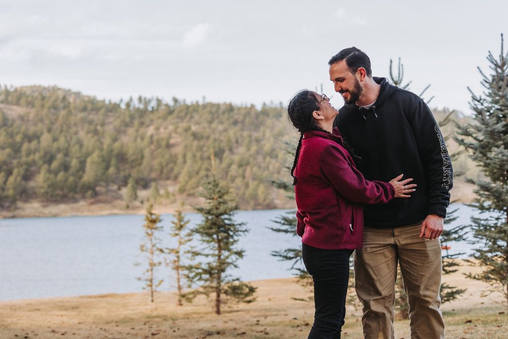 A couple shares an intimate moment during their engagement photoshoot against a scenic mountain lake backdrop.