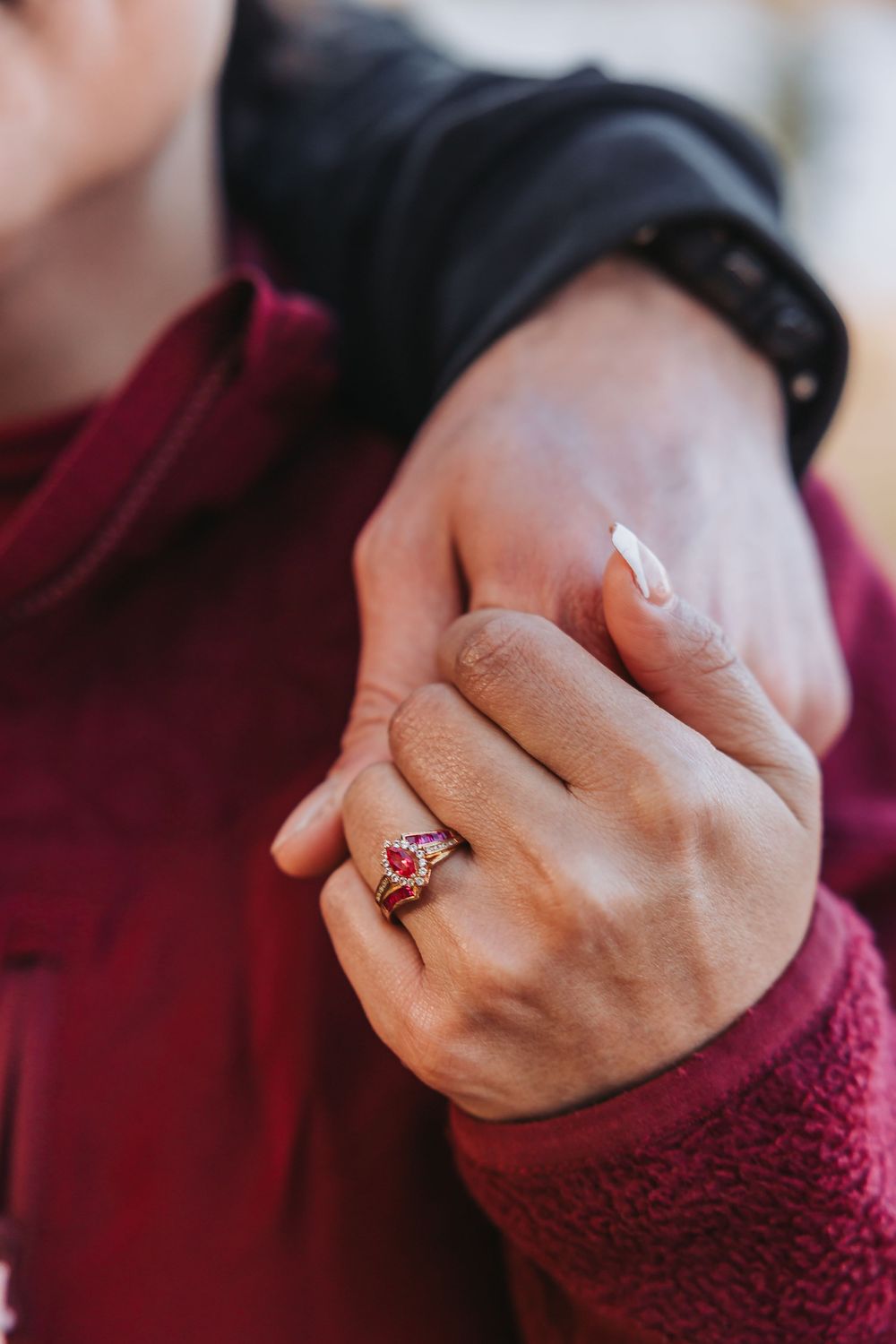 A close-up sequence of hands wearing a burgundy sweater sleeve showing off a pink gemstone ring.