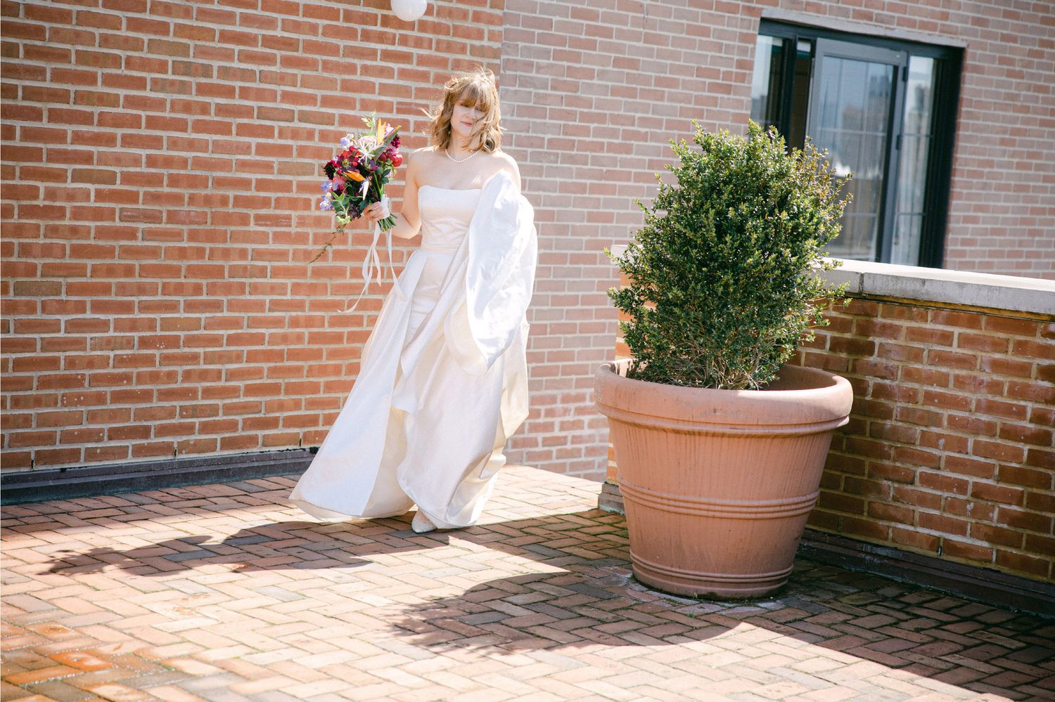 White dress twirling in sunlight against brick wall with potted plants creating a dreamy outdoor scene.