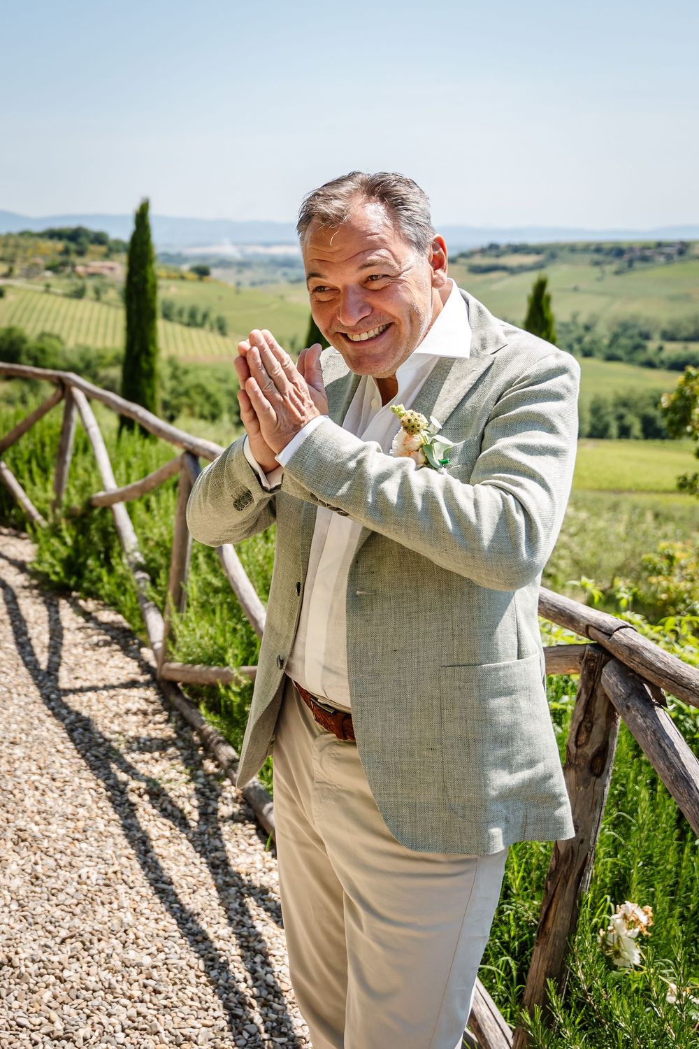 Man in light colored suit laughing joyfully against scenic Tuscan countryside view.