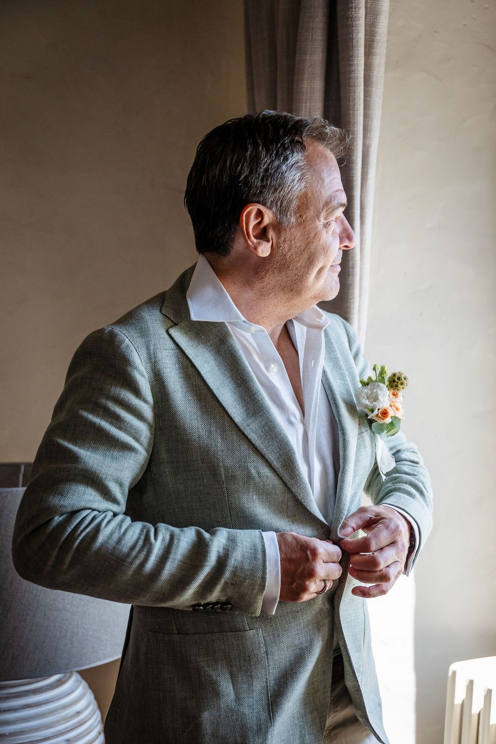 A person in a light gray suit and white shirt gazes thoughtfully out a window.