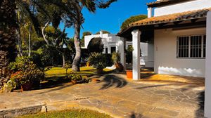 A panoramic view of a Mediterranean-style residential street with white stucco homes and palm trees in sunlight.