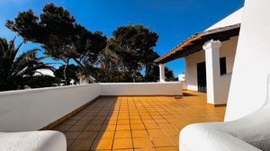 Mediterranean villa terrace with yellow tiled floor and white walls under bright blue sky.