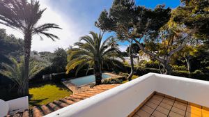 Panoramic view of a Mediterranean coastal villa with palm trees and white architecture overlooking the blue sea.