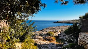 Panoramic view of a rocky Mediterranean coastline with blue sea and clear sky on a sunny day.