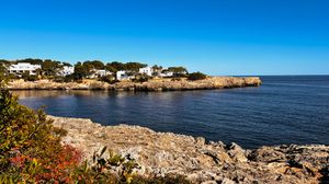 Scenic coastal landscape showing turquoise waters, rocky cliffs and white buildings along the Mediterranean shore.