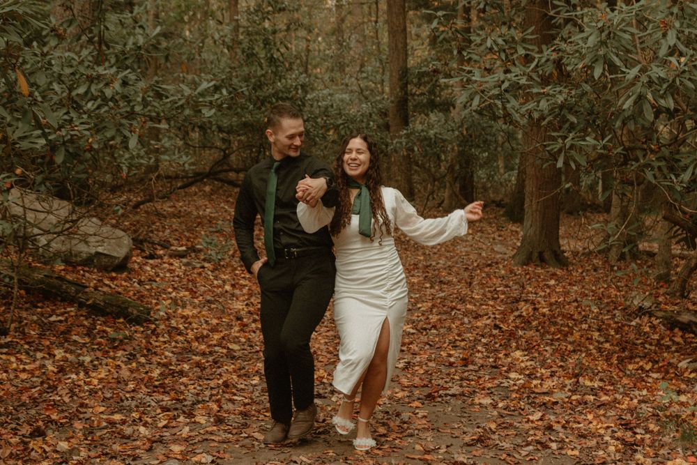 Happy couple laughing together while walking through fallen leaves in a forest.