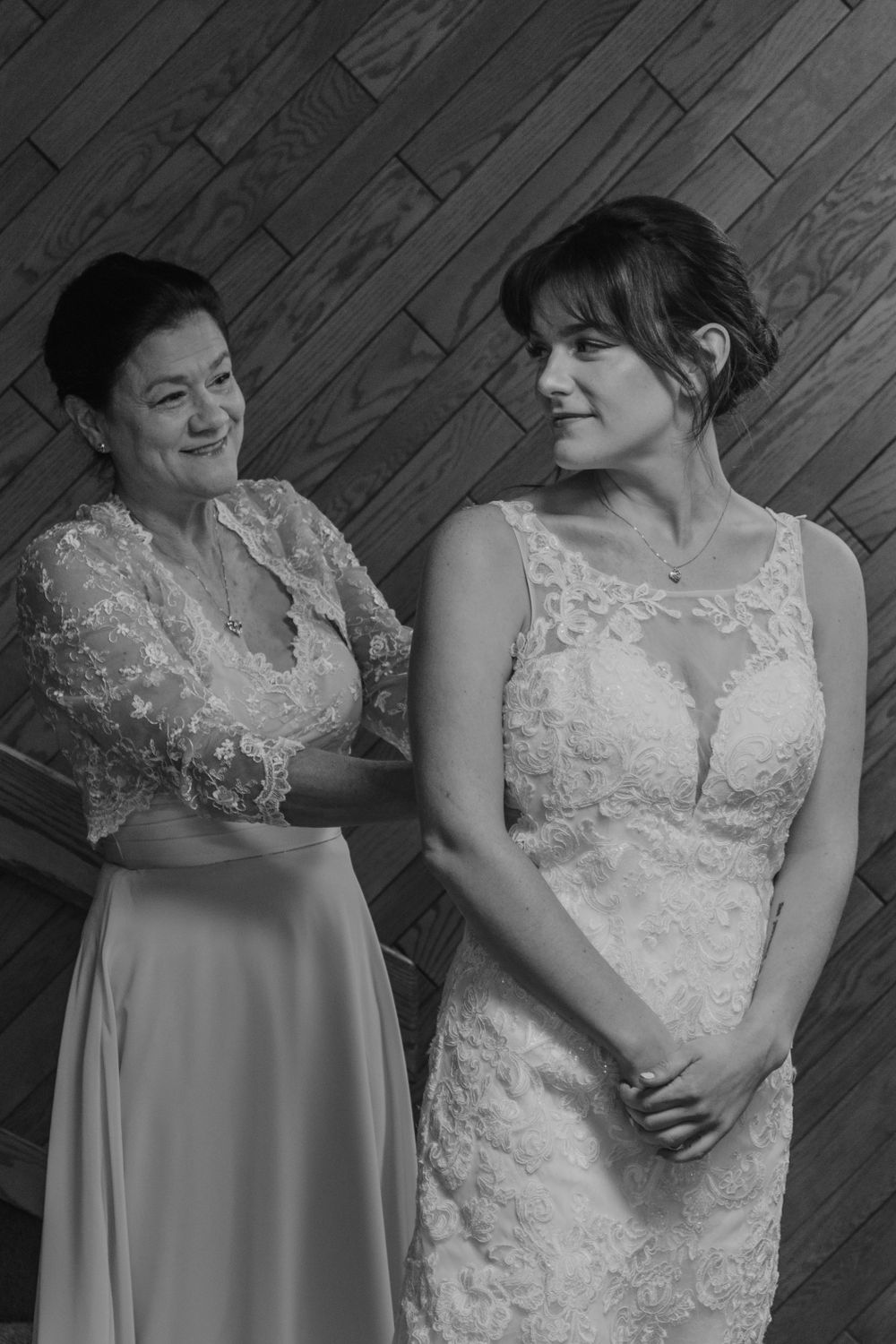 Bride and bridesmaid share candid moments against a rustic wooden wall background.