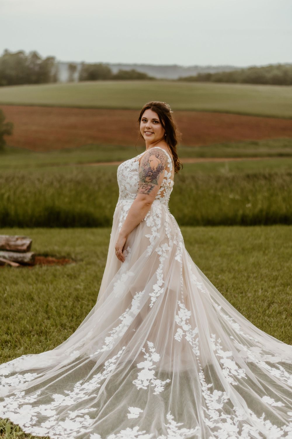 Wedding dress with intricate lace details and flowing train photographed in field.