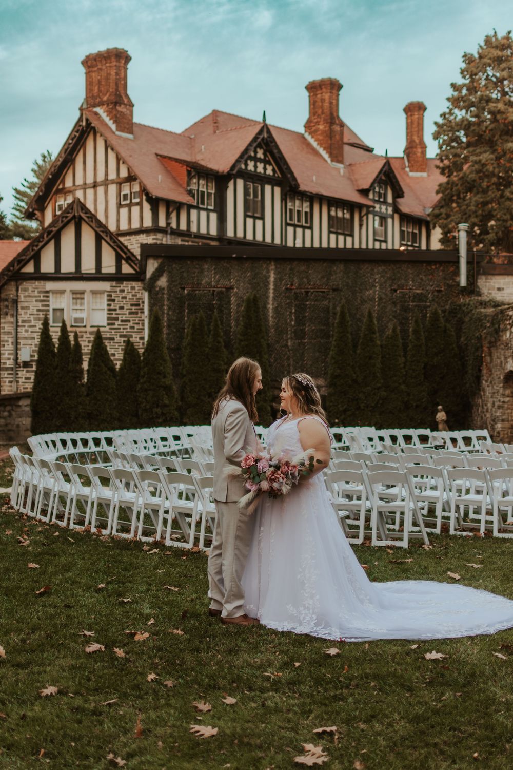 Outdoor wedding ceremony setup with white chairs and Tudor architecture in background.