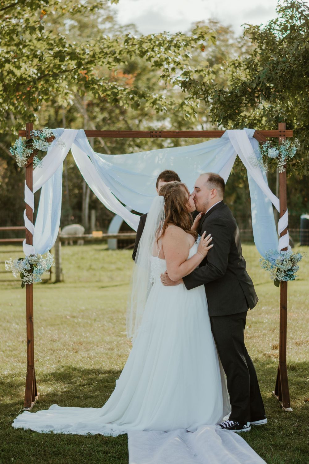 Wedding ceremony setup with flowing white fabric draped on wooden arch in outdoor garden setting.