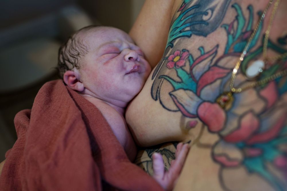 A newborn baby wrapped in a pink blanket rests next to colorful tattoo art.