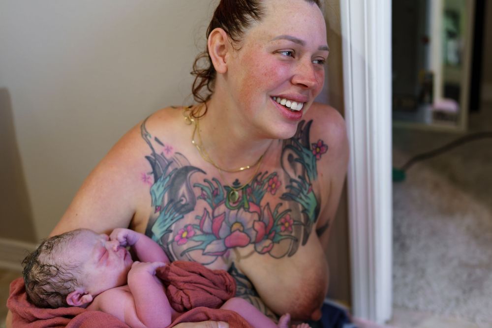 A person with colorful floral tattoos smiles warmly in natural lighting.
