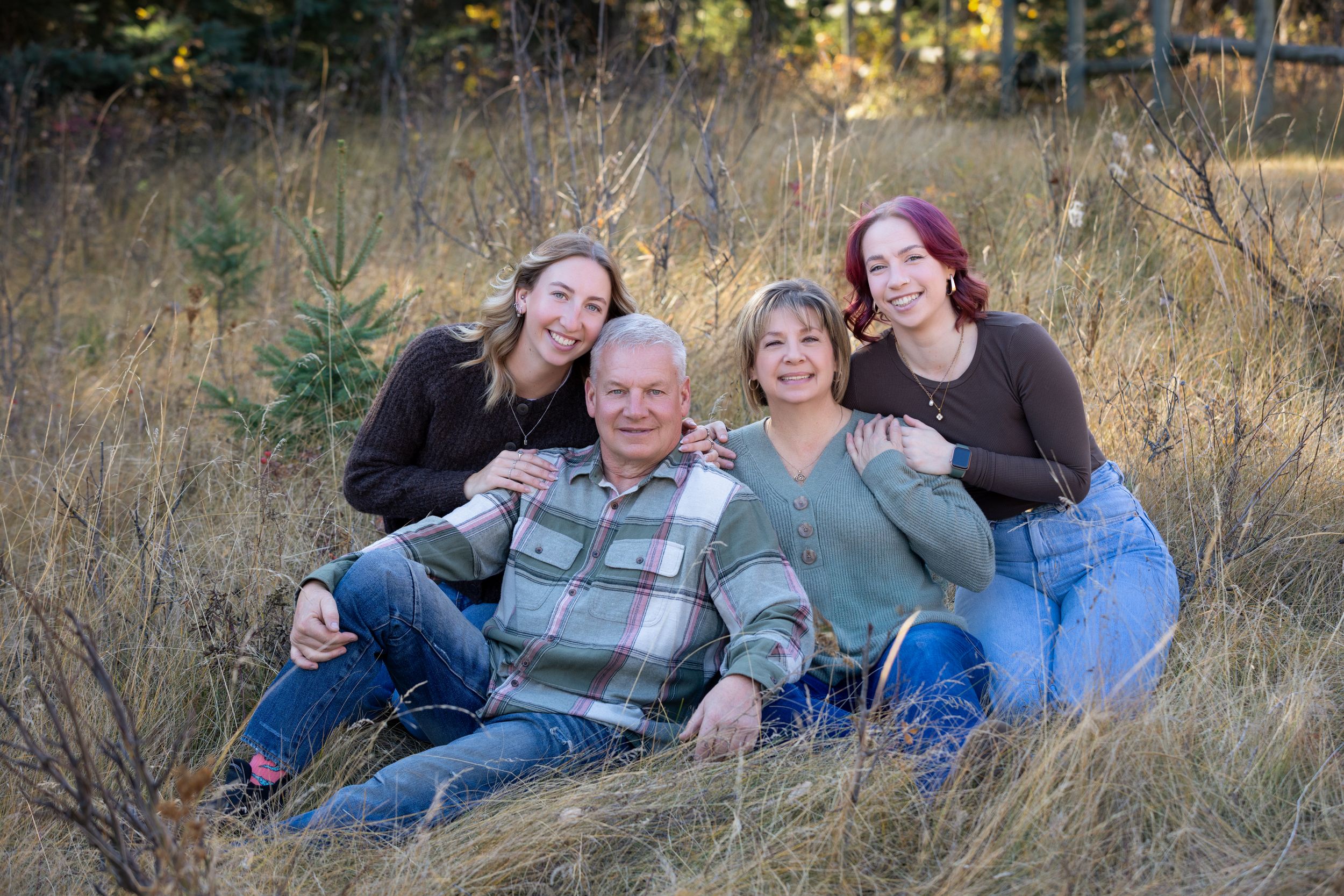 Family members pose together on grassy hillside during outdoor autumn photo session.