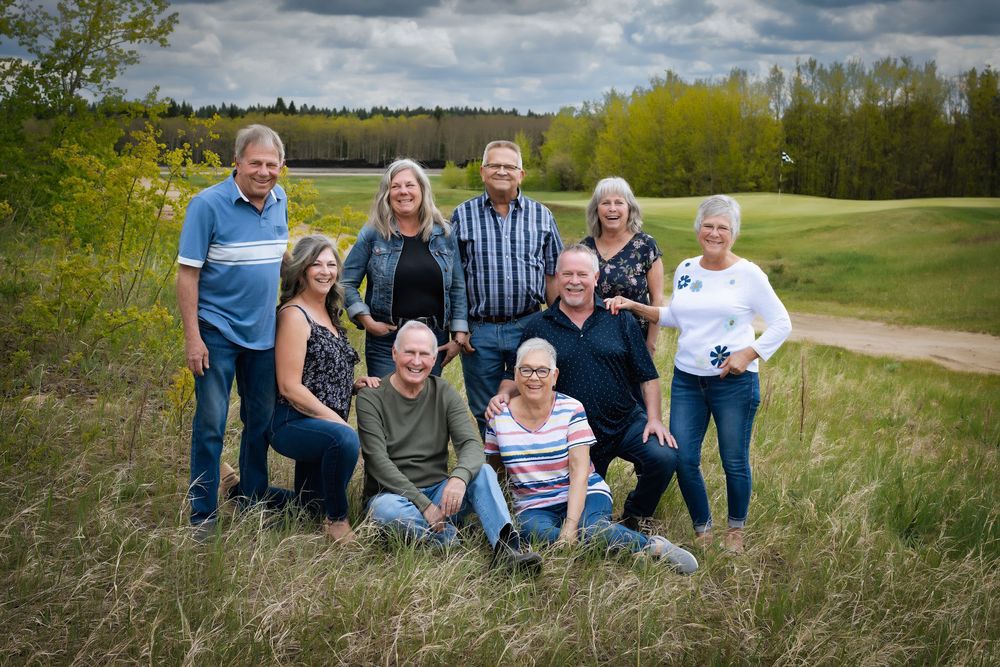 A group of people sitting together outdoors in a grassy field on a sunny day with blue skies and clouds.
