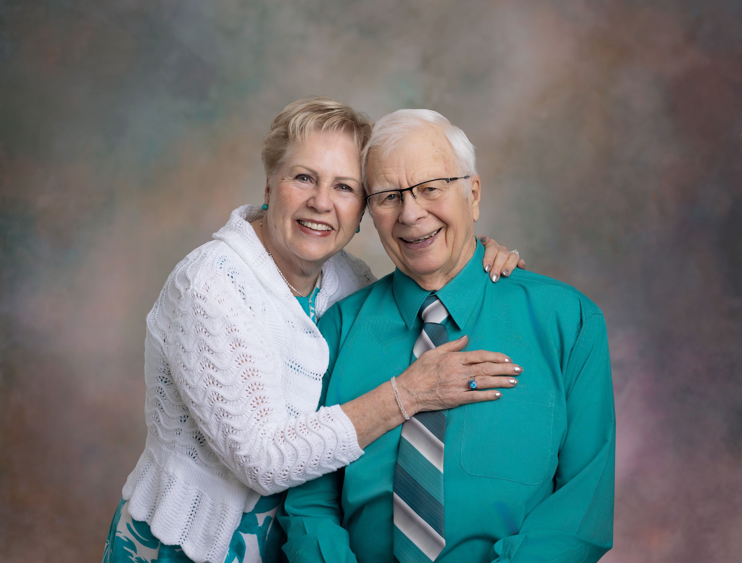 Two people share a joyful moment together while wearing white and turquoise clothing in a studio setting.