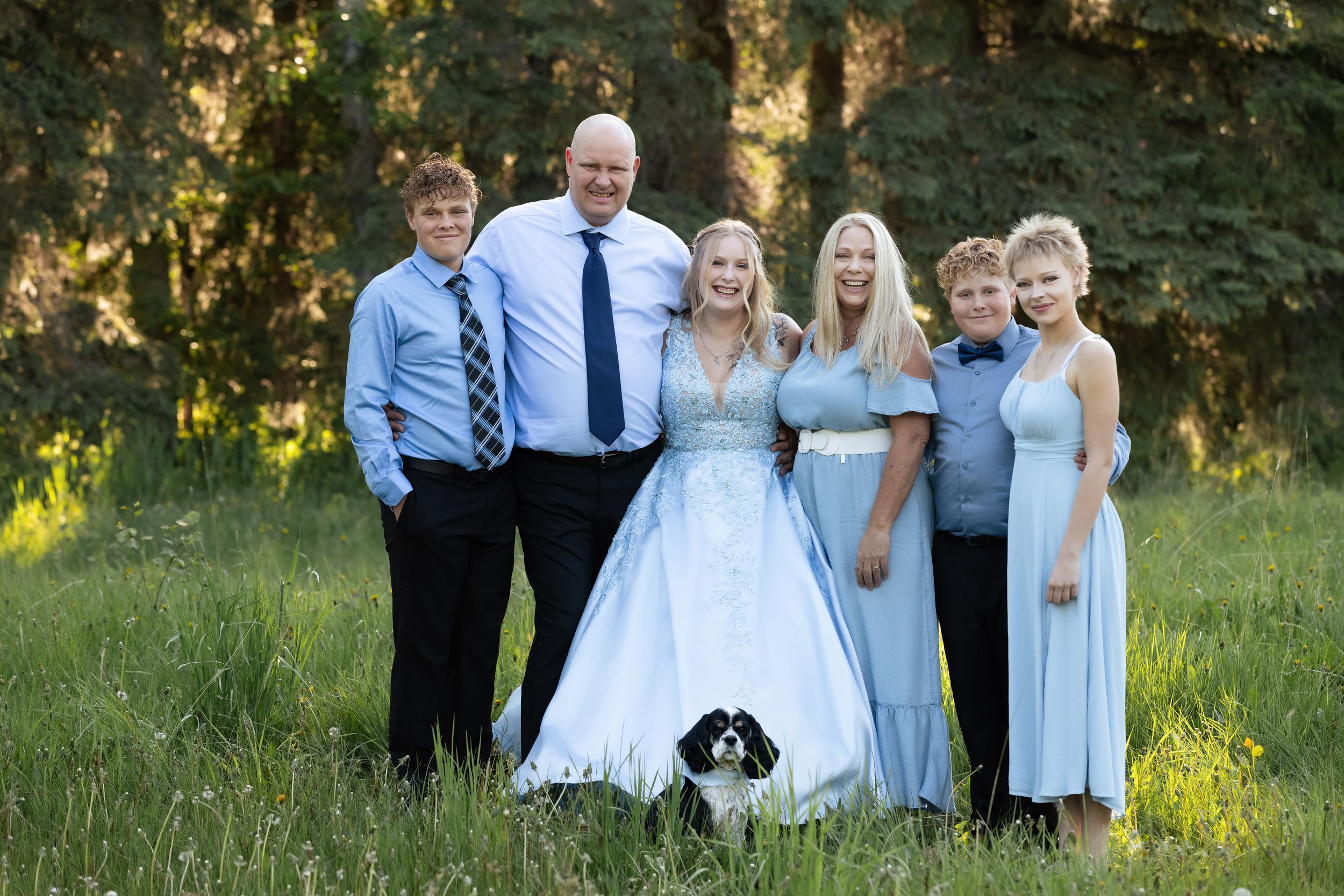 Family group poses together in formal attire on grassy field during golden hour sunset.