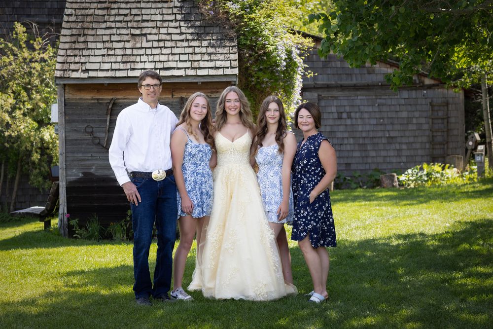 A group of people pose together outdoors in front of a rustic barn wall on a sunny summer day.