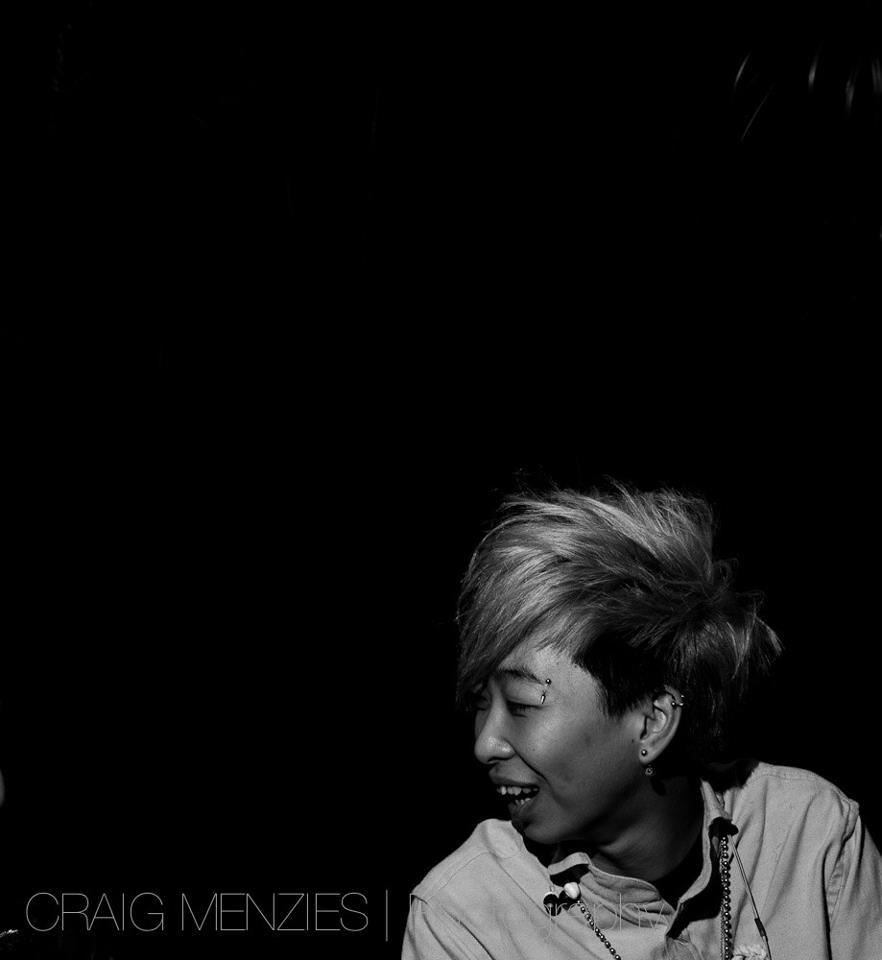 Black and white portrait of a smiling Asian person with short hair in low light.