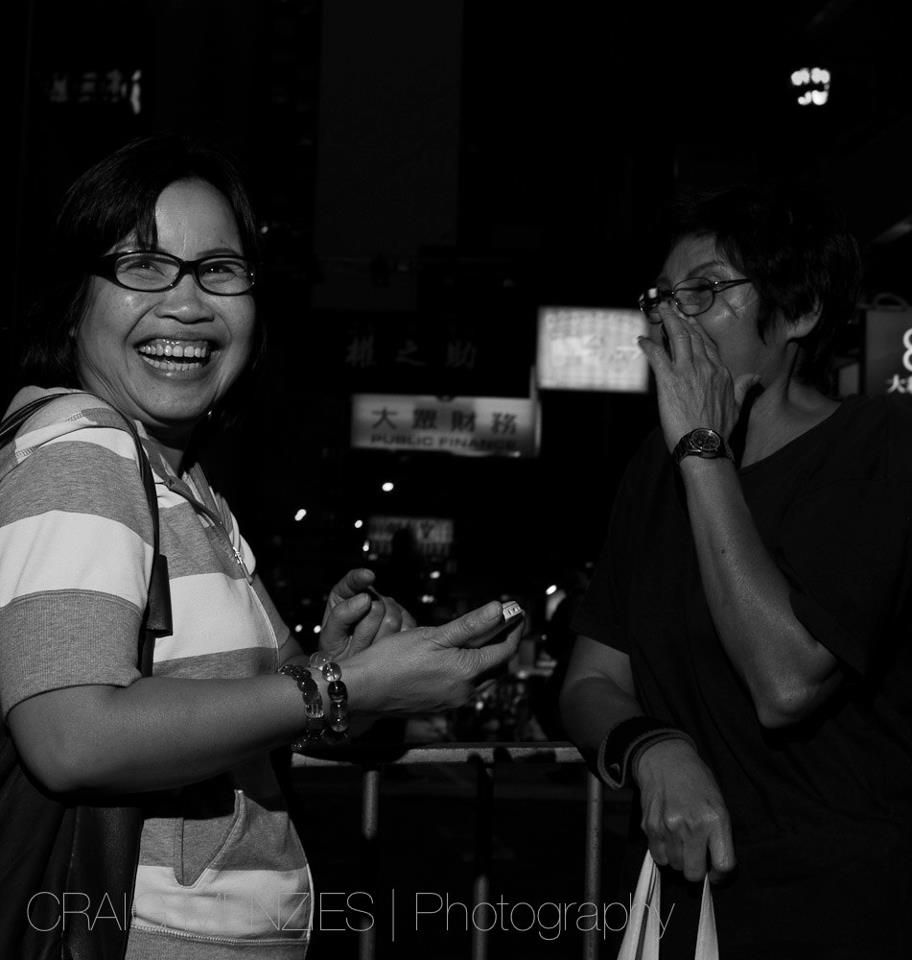 Black and white street photo of two laughing Asian women at night.