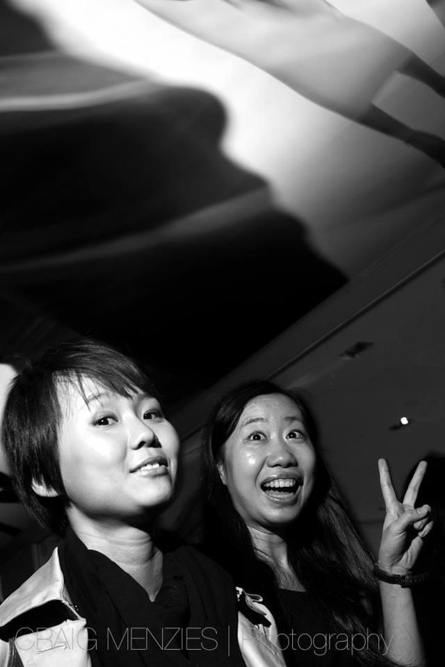 Black and white photo of two Asian women looking up, one making a peace sign.