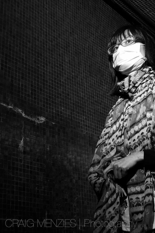 Black and white portrait of a woman wearing a face mask and patterned scarf.
