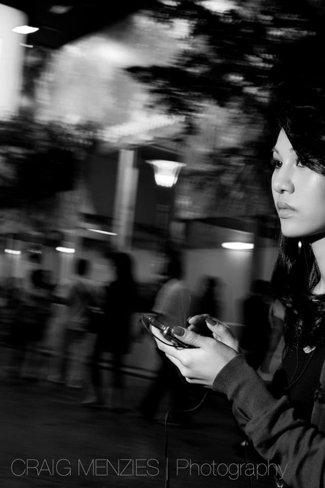 Black and white street photo of a woman looking at her phone at night.