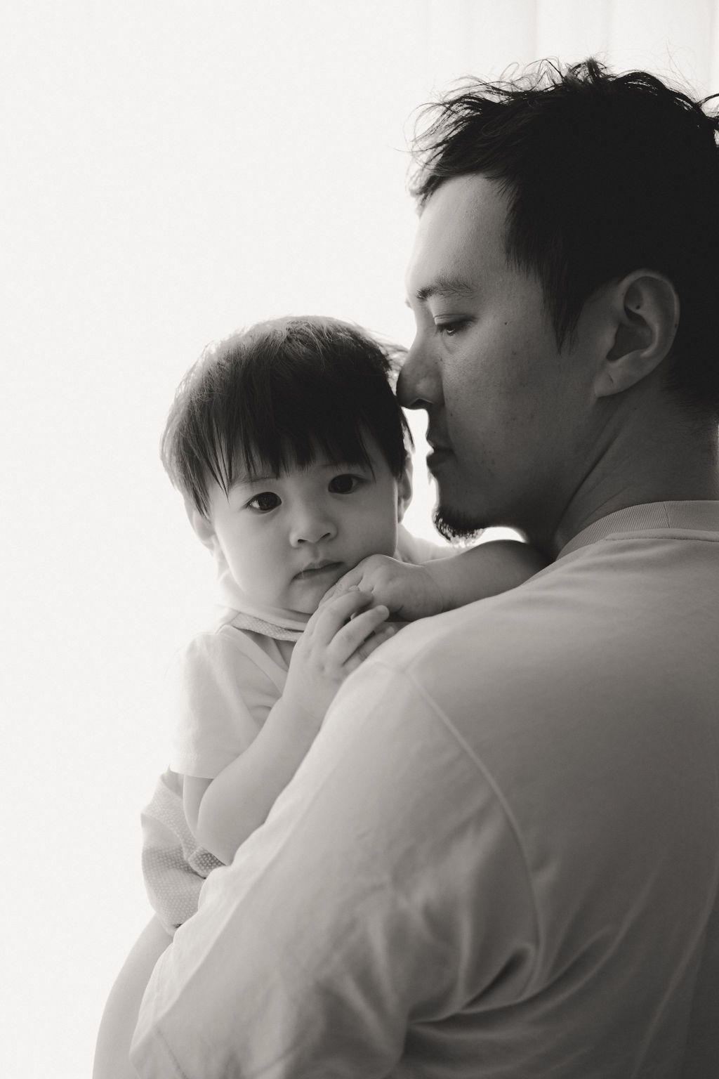 A tender moment between parent and child laying on white bedding in a warm-toned studio setting.在暖色調的攝影棚環境中，父母和孩子躺在白色床單上，享受溫馨的時刻。